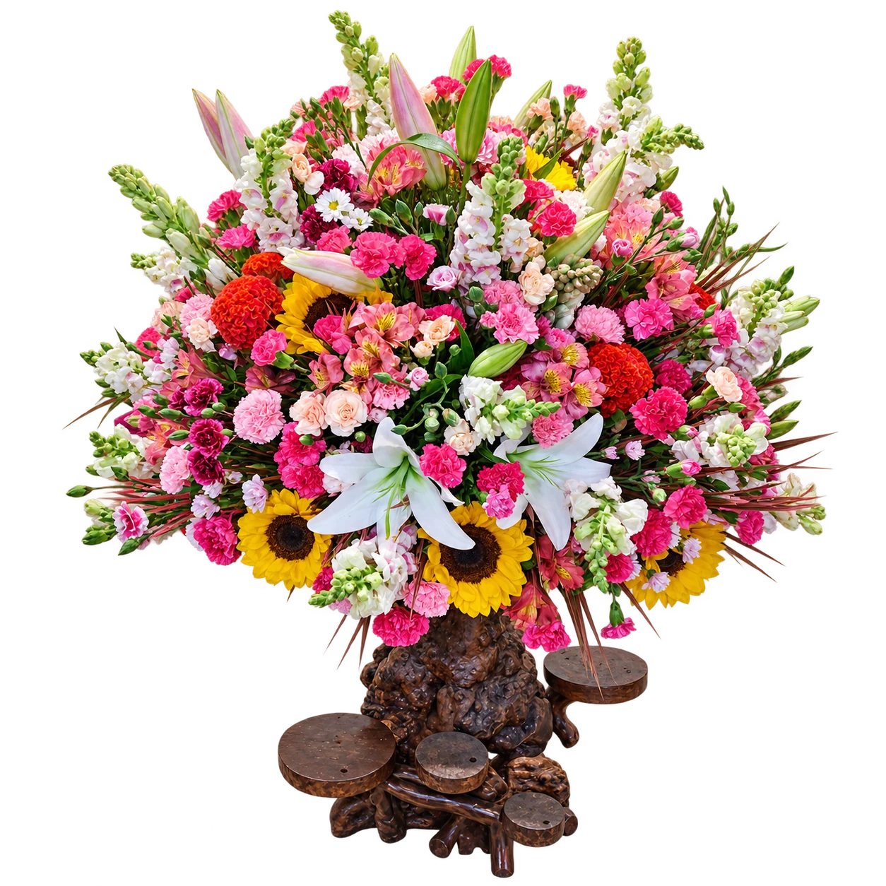 A tall mixed arrangement of pink, red, yellow and white flowers on its sculptural wooden base
